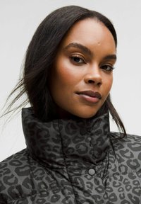 Jachetă puffer neagră, matlasată, cu guler înalt și model cu imprimeu leopard. Dispune de nasturi tip snap și o textură netedă și lucioasă.