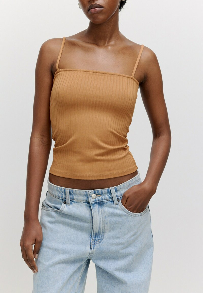 Ribbed braunes Tanktop mit dünnen Trägern, figurbetontem Design und cropped Länge, kombiniert mit hellblauen hochgeschnittenen Jeans.
