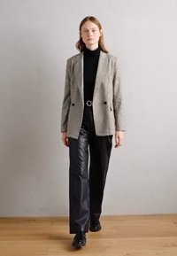 Sacou cu carouri gri peste un pulover negru cu guler înalt, realizat în combinație cu pantaloni de piele negri și pantofi negri. Texturi netede și un design ajustat.