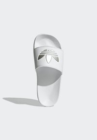 White slide sandal featuring a textured upper with a cut-out logo design. Flat sole with rounded toe and cushioned footbed for comfort.