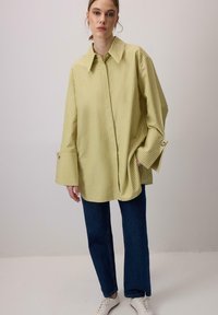 Kollase triibuga oversized särk terava kraega ja laiade varrukatega. Sobitatud tumepruunide teksade ja valgete tossudega.