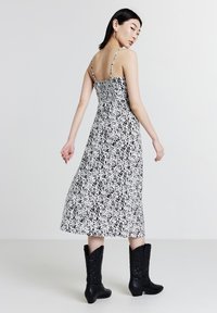 Donna che si volta indossando un abito midi a pois bianco e nero con spalline sottili e stivali neri ricamati fino al polpaccio.