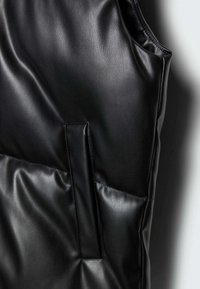 Chaleco de cuero negro con una textura suave y un diseño acolchado. Los detalles notables incluyen un bolsillo lateral y sutiles acentos de costura.