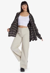 Czarna i beżowa koszula w kratę oversize, biała bluzka crop top oraz beżowe szerokie spodnie z kordurowego materiału. Czarna sneakersy dopełniają outfit.