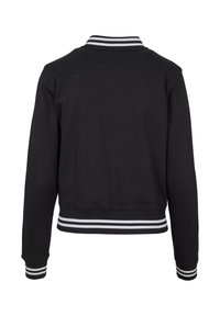 Veste bomber noire à manches longues avec col, poignets et ourlet côtelés avec deux bandes blanches, vue de dos sur fond blanc.