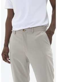 Pantalones gris claro confeccionados con tejido texturizado, con cierre de botón en la parte delantera y bolsillos laterales, combinados con una camiseta blanca.