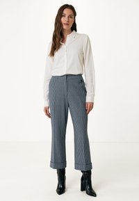 Camicia bianca a maniche lunghe abbinata a pantaloni a vita alta a quadri blu e bianchi, con design dritto e orli risvoltati. Stivaletti neri alla caviglia.