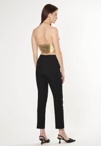 Top senza spalline in oro metallizzato abbinato a pantaloni attillati neri; entrambi presentano texture lisce, linee pulite e un design minimalista.