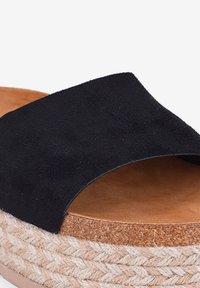 Scarpe slip-on in suede nero con una tomaia ampia, dotate di una suola a zeppa in sughero naturale e juta. Fodera interna liscia.