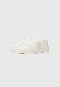 Sneakers bianchi in tela con punta rotonda, lacci piatti e un logo sottile. Presentano una texture liscia e un design minimalista.