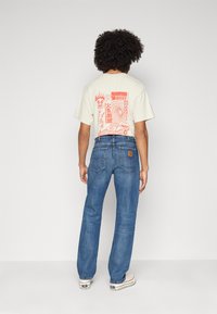 Light beige t-shirt with red graphic print on the back, paired with blue straight-leg jeans and white sneakers. Classic denim style.
