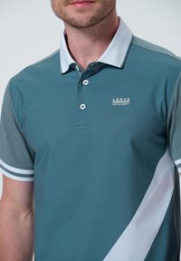 Teal polo skjorta med vit accent och grå ärmar. Tre knappar vid kragen, med en liten "Luhta Sport" logotyp på bröstet.