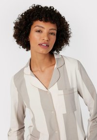Top in cotone leggero con strisce verticali beige e bianche, colletto a punte, tasca sul petto e piping dorato lungo le cuciture.