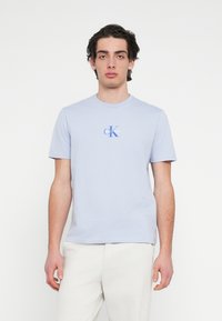 Ανοιχτό μπλε βαμβακερό μπλουζάκι με κοντά μανίκια, στρογγυλή λαιμόκοψη και μικρό λογότυπο "CK" σε μπλε και λευκό στο στήθος. Λεπτή υφή.