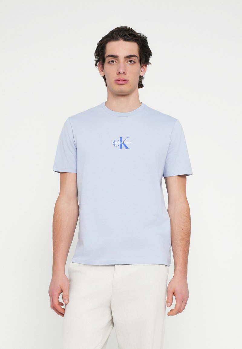 Ανοιχτό μπλε βαμβακερό μπλουζάκι με κοντά μανίκια, στρογγυλή λαιμόκοψη και μικρό λογότυπο "CK" σε μπλε και λευκό στο στήθος. Λεπτή υφή.