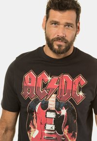 Camiseta negra con un gráfico de guitarra eléctrica roja con llamas. El texto dice "AC/DC" en letras grandes y desgastadas en la parte delantera.