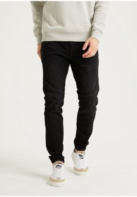 Los jeans negros entallados presentan una textura suave con paneles detallados. Combinados con zapatillas blancas que tienen detalles en beige.