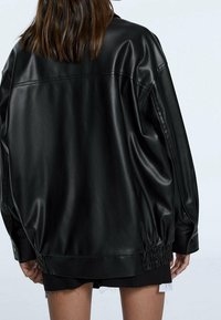 Oversized zwart faux lederen jas met een zachte textuur, elastische gerimpelde zoom en drukknoopdetails op de manchetten.
