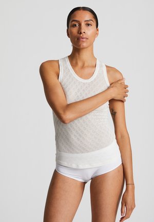 Balta nėriniuota liemenėlė su tekstūruota deimanto rašto, apvaliu iškirpimu. Minkšta medžiaga ir prigludusi fasonas. Atitinkami balti šortai po ja.