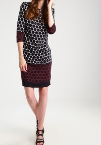 Mustikka-valkoinen pilkullinen mekko, jossa on kolme neljännesosa hihat, ja siinä on tiukka hame, jonka helmassa on punainen ympyräkuvio. Teksturoitu kangas.