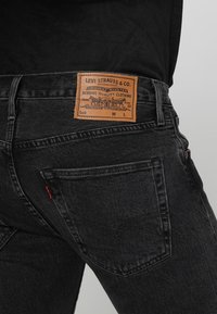 Svarta denimjeans med en läderlapp med "Levi Strauss & Co." präglat. Traditionell fickdesign med en röd etikett på bakfickan.