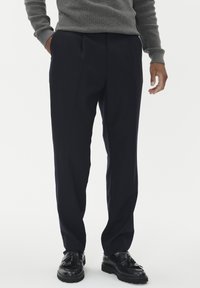 Mornarske hlače ravnog kroja, s jednim nabranim detaljem i glatkom teksturom. Uparene s crnim cipelama s detaljem kopče.