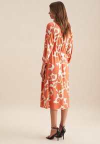 Kleider mit Halbärmeln und floralem Muster in Koralle und Weiß, mit gerafftem Taillenbund und fließendem, knöchellangem Rock. Tragen Sie dazu schwarze Absätze.