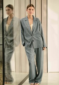 Blauw geblokt pak in een relaxte pasvorm, bestaande uit een blazer met knopen en brede broekspijpen. Glad materiaal met een geometrisch ontwerp en lichte accenten.