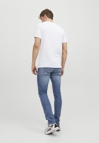 T-shirt bianco in cotone, jeans blu e scarpe da ginnastica. L'outfit presenta un design semplice con una silhouette aderente e denim in lavaggio chiaro.