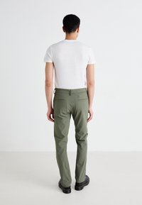 Olive green slim-fit trousers with a smooth texture, featuring two back pockets and a standard waistband, worn with a white t-shirt.