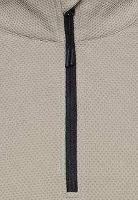 Beige Texturierter Stoff mit einem halben Reißverschluss vorne, ausgestattet mit einem schwarzen Reißverschluss. Die Oberfläche hat ein Rautenmuster, das Tiefe und visuelles Interesse verleiht.