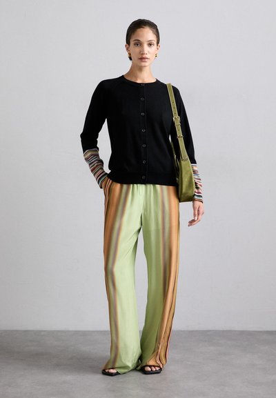 Cardigan nero con chiusura a bottoni e maniche a righe multicolori, abbinato a pantaloni a righe verdi con accenti arancioni e marroni.