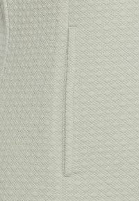 Světle šedá, texturovaná látka s diamantovým vzorem; obsahuje boční kapsu; měkký, tkaný textil s hladkým povrchem.