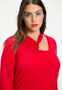 Rode lange mouwen top met een geknotte detail bij de halslijn en een vierkante uitsnijding. Gemaakt van een gladde, rekbare stof.