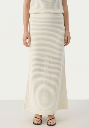 Jupe maxi en tricot blanc avec un motif texturé, dotée d'une taille ajustée et d'une fente latérale, associée à des sandales noires à lanières.