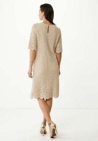 Beige spetsklänning med korta ärmar och scallopkant, med en nyckelhålsslit i ryggen. Bärs med guld höga klackar.