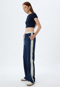 Marineblå cropped top og løse bukser med lyse vertikale striber og elastisk talje. Inkluderer sidelommer og hvide sneaker.