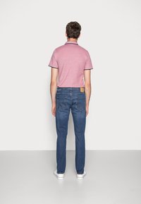 Camisa de polo rosa con ribetes azul marino, combinada con jeans azules con bolsillos traseros y un parche de cuero con logo, zapatos en blanco.