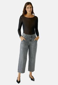 Schwarzer, transparenter Langarm-Body mit Punkten, kombiniert mit hochtaillierten, ausgebleichten grauen, weiten Jeans mit Fronttaschen und abgeschnittenen Details.