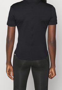 Svart atletisk kortärmad topp med figurnära passform, tillverkad av mjukt tyg. Har sydda sömmar och en rundad fåll.