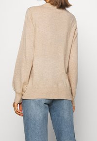 Pull beige léger à col rond, avec épaules tombantes, ourlet côtelé et manches longues, associé à un jean bleu clair.