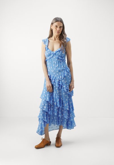 Blue, tiered dress in lightweight fabric with ruffled accents and small white floral patterns. Paired with brown lace-up shoes.