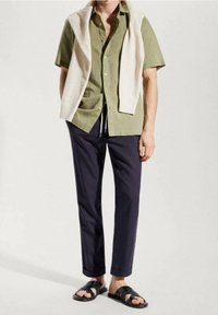 Camicia verde a maniche corte con bottoni, maglione crema drappeggiato sulle spalle, pantaloni navy a gamba affusolata e sandali neri con più cinturini.