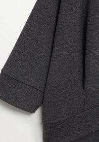 Tissu gris foncé avec une texture douce, présentant un design légèrement ample et des manches larges, terminé par un simple poignet replié.