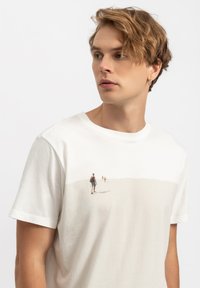 Wit katoenen t-shirt met korte mouwen, voorzien van een grafisch ontwerp van een strandscène in subtiele kleuren op de borst. Soepele textuur en een comfortabele pasvorm.