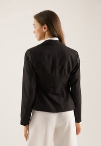 Schwarzer taillierter Blazer mit strukturiertem Schnitt, Reverskragen und langen Ärmeln, der eine glatte Textur und ein dezentes Rückennahtdetail aufweist.