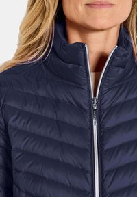 Marineblauwe geïsoleerde jas met een hoge kraag en een quiltpatroon. Beschikt over een volle rits aan de voorkant en een gladde textuur.