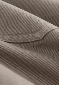 Tessuto beige con una fine trama, caratterizzato da un delicato motivo a diagonale e da un bordo cucito, che conferisce un aspetto liscio e drappeggiato.