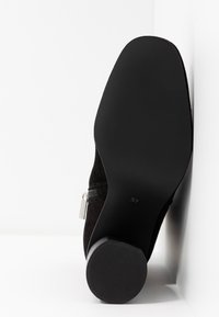 Bottine en suedé noir avec un bout arrondi, une fermeture éclair latérale, une semelle en caoutchouc noir texturée et un petit talon carré. Taille 37 indiquée sous la semelle.