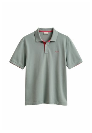 Polo vert clair à manches courtes avec doublure rouge à l'intérieur du col, patte de boutonnage à un seul bouton et petit logo rouge sur la poitrine.